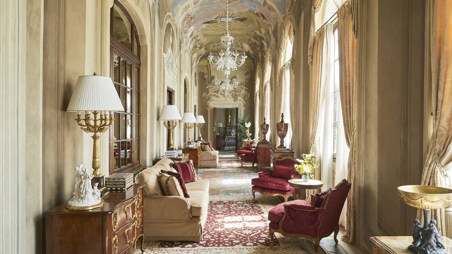 Grand, arched hallway with frescoed ceiling and chandelier, lounge seating and ruby-red arm chairs, in the Royal Suite at Four Seasons Hotel Florence